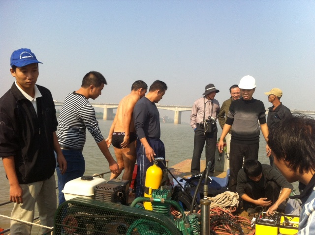 Trên xà lan, mọi người chăm chú chuẩn bị để thợ lặn xuống đáy sông Hồng tìm kiếm 