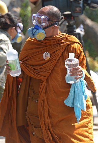 Một nhà sư Thái đeo kính và mặt nạ chống hơi cay chuyên dụng, tay cầm chai nước muối đến với người biểu tình.