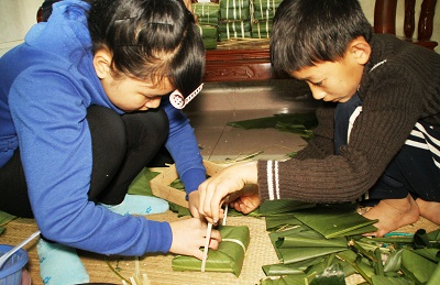 Các anh chị lớn hướng dẫn em nhỏ gói bánh.