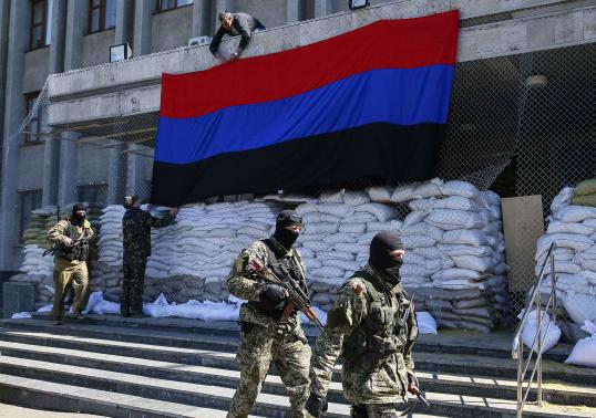 Pro-Russian armed men walk past activists hanging up a Donetsk Republic flag outside the mayors office in Slaviansk, April 21, 2014. REUTERS-Gleb Garanich