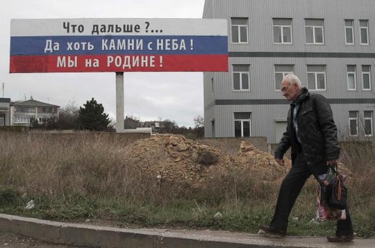 A man carries a bag attached with an orange and black ribbon of St. George as he walks past a billboard in the Crimean port of Sevastopol, November 29, 2014. The billboard reads: Whats next? At least the stones are from the sky! We are at home! REUTERS/Pavel Rebrov