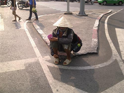 Một người đàn ông khỏe mạnh, lành lặn, đội nón lá lụp xụp cố tình che giấu khuôn mặt... còn trẻ ngồi chờ bố thí tại ngã tư Bảy Hiền (quận Tân Bình)
