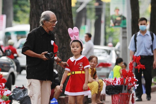 Một cụ già dẫn cháu gái trong trang phục xinh xắn đi chụp ảnh Noel