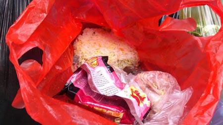 Túi nilon chứa 2 đĩa xôi, cá và thịt vụn bị đổ vào thùng rác. Ảnh: Lê An