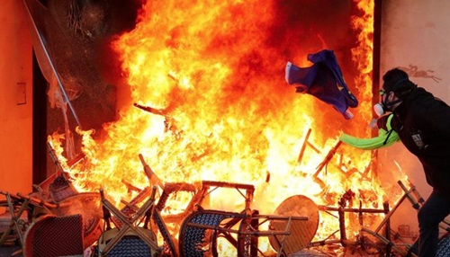 Người biểu tình ném lá cờ vào đám cháy tại một cửa hàng ở Paris hôm 16/3. Ảnh: Reuters.