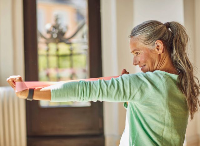 người phụ nữ trưởng thành tập bài tập cánh tay bằng dây kháng lực tại nhà, khái niệm về bài tập giảm cân cho người lớn trên 50 tuổi