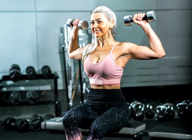 người phụ nữ trưởng thành, cân đối và mạnh mẽ cầm tạ uốn cong cơ bắp tại phòng tập thể dục, khái niệm về các bài tập để tăng sức mạnh phần trên cơ thể khi bạn già đi
