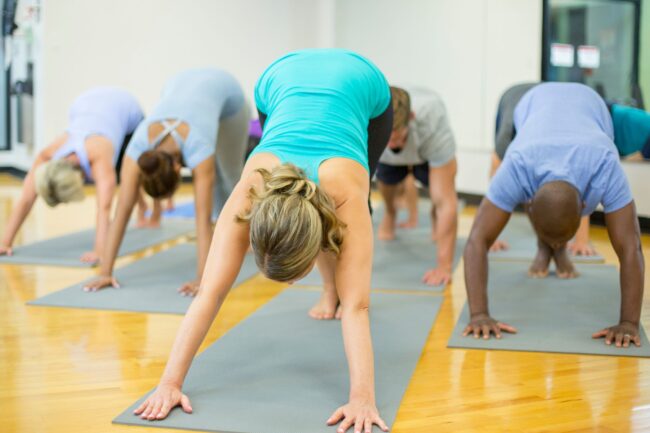 Mọi người đang thực hiện tư thế chó úp mặt trong phòng tập yoga. Bài tập kéo giãn này nhắm vào gân kheo và bắp chân, là lựa chọn tuyệt vời để làm giảm các triệu chứng giãn tĩnh mạch