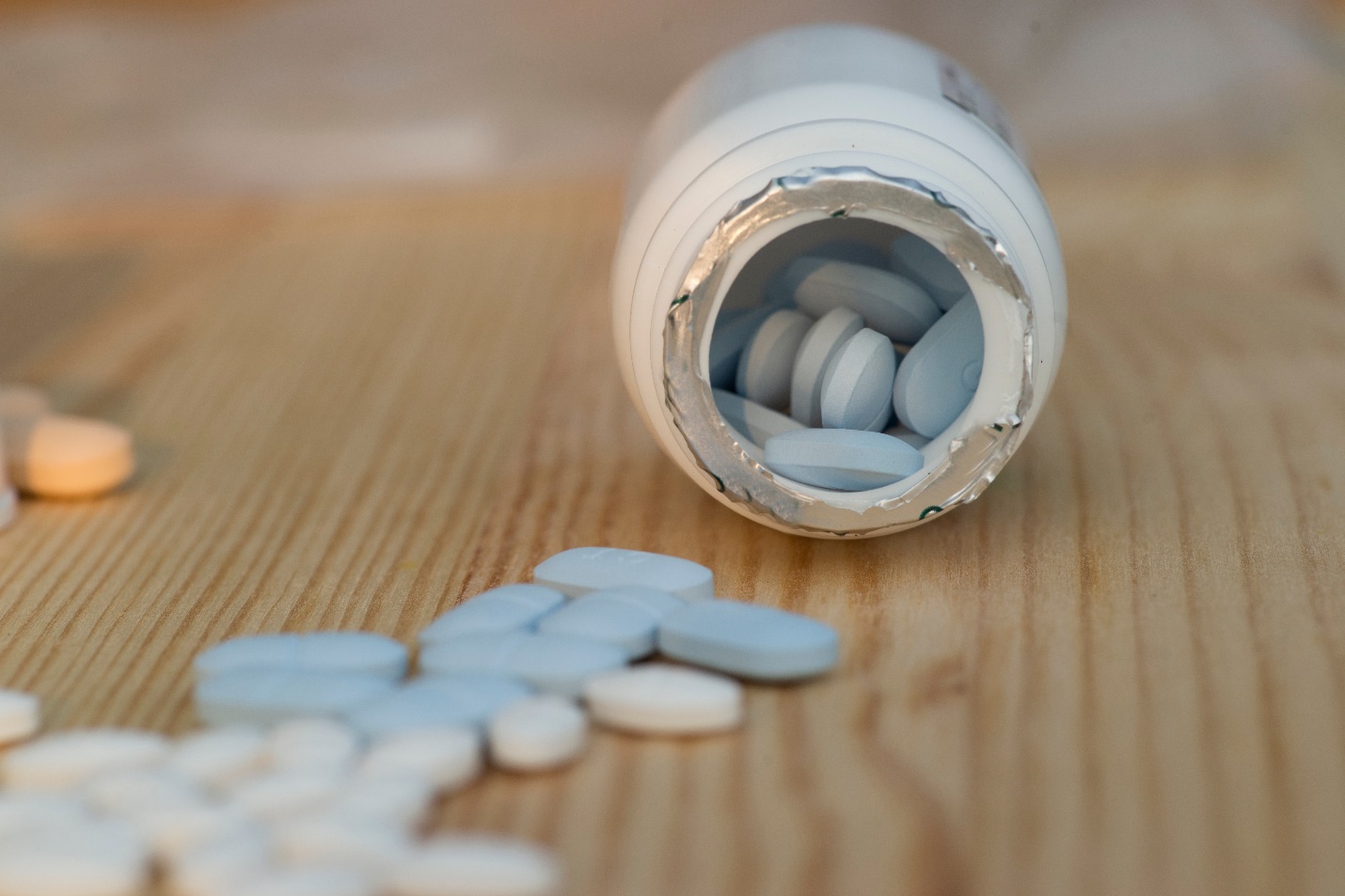 Một lọ thuốc màu trắng trên nền gỗ với những viên thuốc màu xanh và trắng.