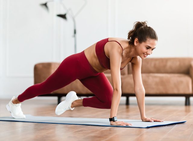 7 động tác đốt cháy mỡ bụng và tăng cơ nhanh hơn cả chạy bộ- Ảnh 4. Smiling Sporty Woman Training At Home In Living Room In Front Of Laptop, Beautiful Female Doing Cross Body Mountain Climbers Exercise Looking At Screen Having Online Video Call With Trainer Instructor