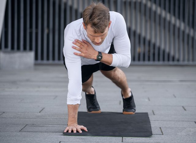 5 bài tập giúp nam giới giữ vóc dáng trẻ trung- Ảnh 6. Full length view of young sportsman doing shoulder tap in push or press ups exercise, standing in plank position. Athlete with smartwatch training outdoors, warm up body, working out on yoga mat