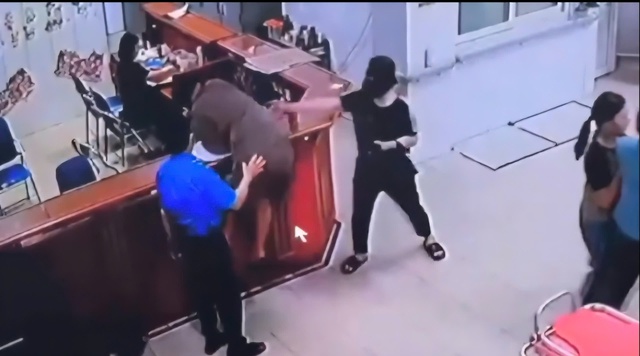 Hình ảnh người đàn ông chồm qua quày làm thủ tục để hành hùng nhân viên y tế. Ảnh cắt từ clip. Hình ảnh người đàn ông chồm qua quày làm thủ tục để hành hùng nhân viên y tế. Ảnh cắt từ clip.