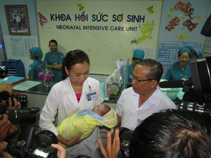 Bé sơ sinh được đưa ra gặp cha trong vòng tay của ThS-BS Phạm Thị Thanh Tâm, Trưởng khoa Hồi sức sơ sinh (phải) và TS-BS Nguyễn Thanh Hùng, Giám đốc BV Nhi Đồng 1
