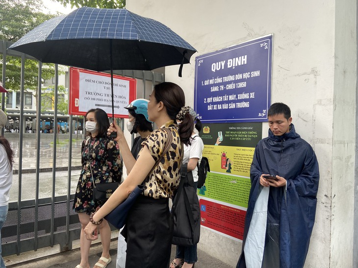 Phụ huynh lặng lẽ "dầm mưa" ngồi đợi con thi tốt nghiệp THPT - Ảnh 1. Phụ huynh lặng lẽ "dầm mưa" ngồi đợi con thi tốt nghiệp THPT - Ảnh 1.
