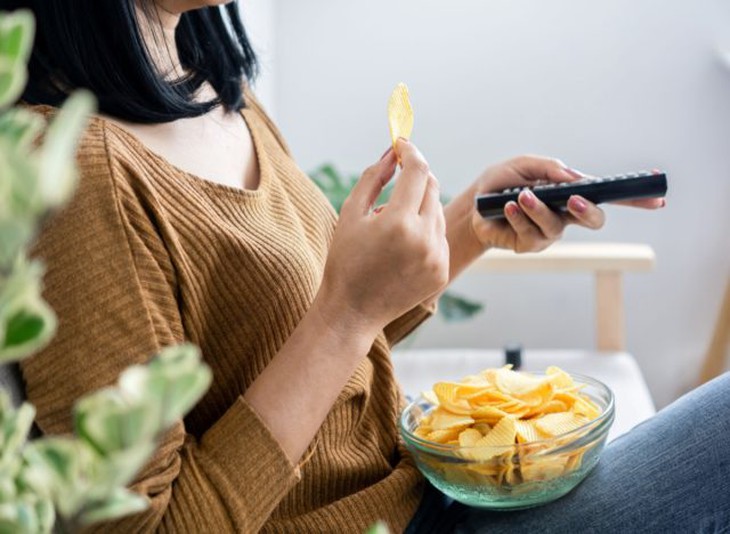 người phụ nữ ăn khoai tây chiên trong khi xem tivi