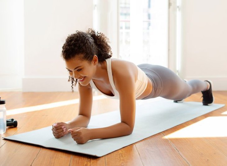 Người phụ nữ trẻ tập thể dục mặc đồ thể thao đang tập plank khuỷu tay để tăng cường sức mạnh cốt lõi trên thảm tập thể dục trong phòng khách hiện đại tại nhà. Khái niệm tập luyện lành mạnh trong nhà, giữ plank.