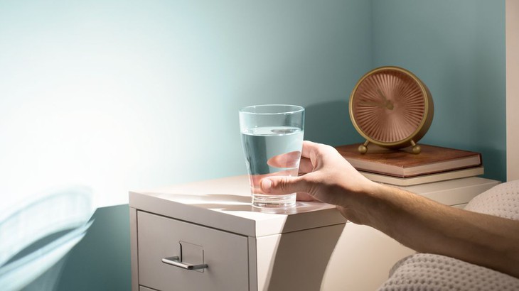 bàn tay với lấy cốc nước bàn cạnh giường buổi sáng